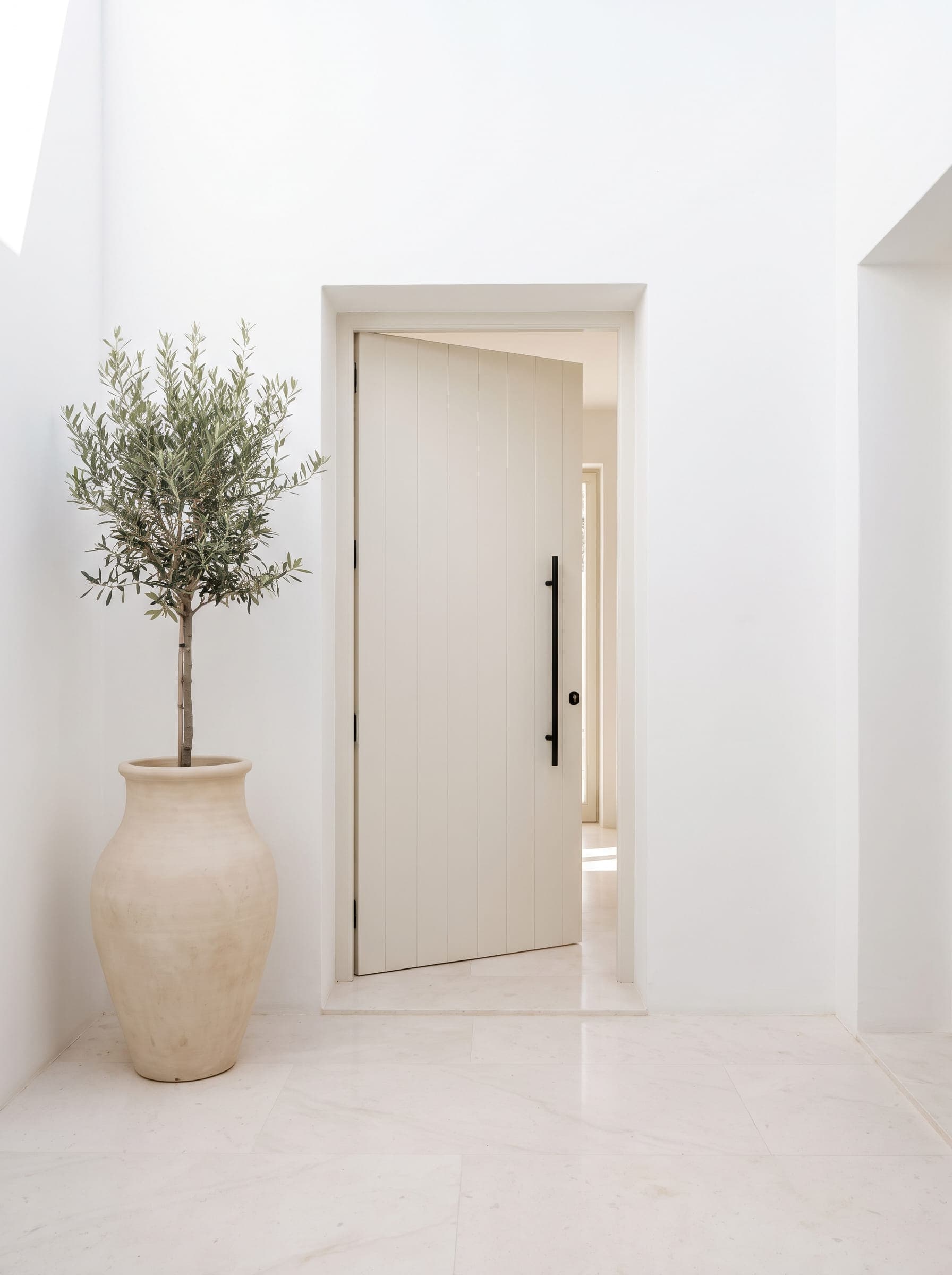 The open front door of a bright, newly finished holiday rental, an olive tree in a pot beside it